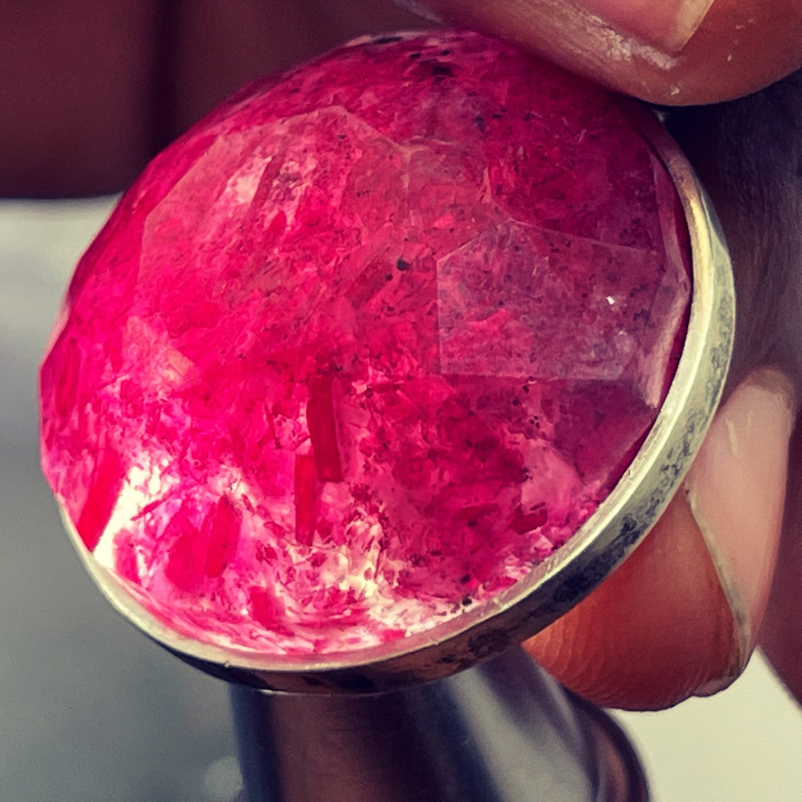 Faceted red stone in a silver bezel held between fingers